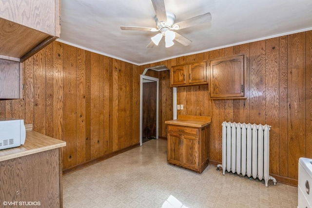 kitchen featuring light floors, arched walkways, brown cabinetry, and radiator heating unit