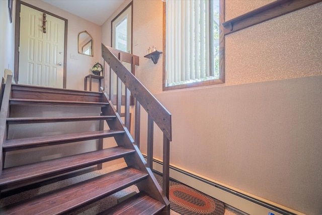 stairway featuring a baseboard heating unit and a healthy amount of sunlight