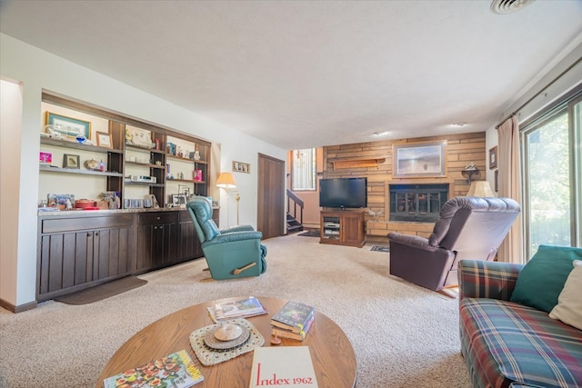 carpeted living room featuring wood walls and a large fireplace