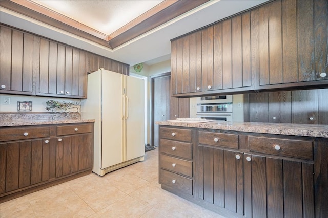 kitchen featuring dark brown cabinets, light stone counters, white fridge, and stainless steel oven