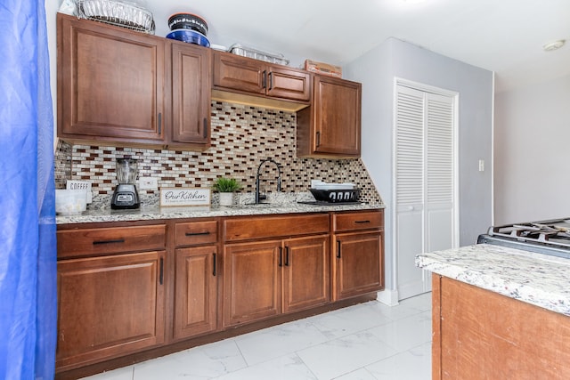 kitchen with light tile patterned flooring, backsplash, light stone countertops, and sink