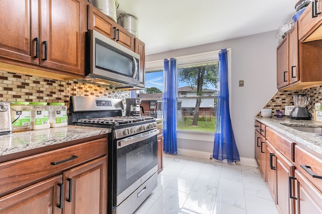 kitchen with a wealth of natural light, light tile patterned floors, backsplash, stainless steel appliances, and light stone countertops