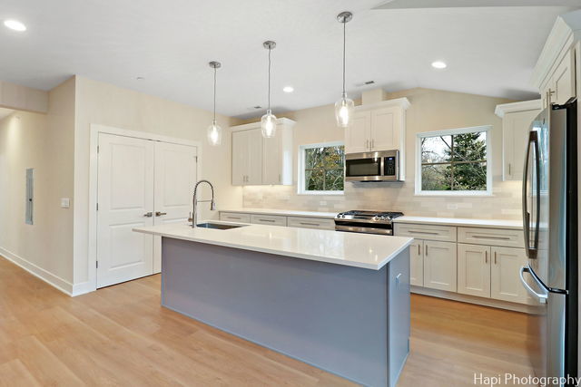 kitchen featuring a center island with sink, decorative light fixtures, white cabinets, and stainless steel appliances