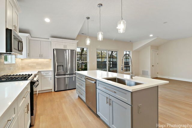 kitchen with stainless steel appliances, sink, decorative light fixtures, a center island with sink, and white cabinetry