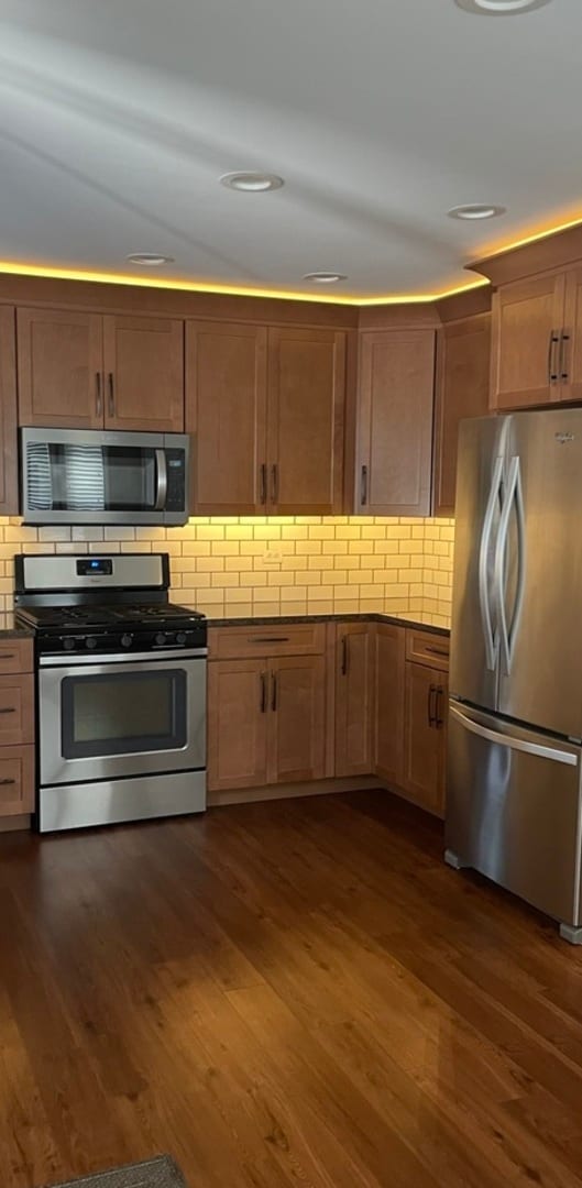 kitchen with appliances with stainless steel finishes, dark hardwood / wood-style floors, and decorative backsplash