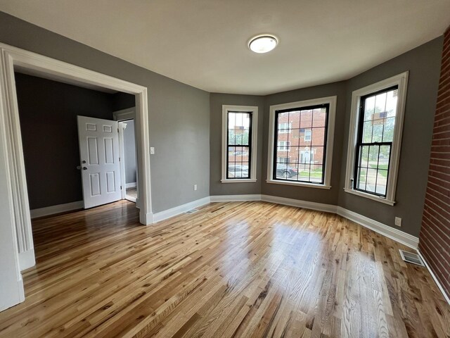 empty room with brick wall, wood-type flooring, and a healthy amount of sunlight