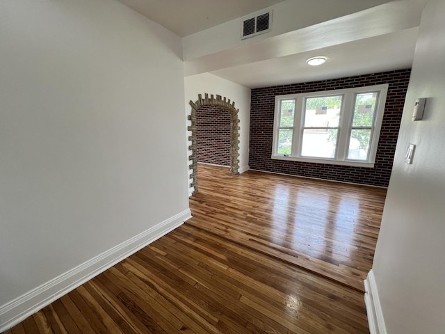 empty room with brick wall and hardwood / wood-style floors