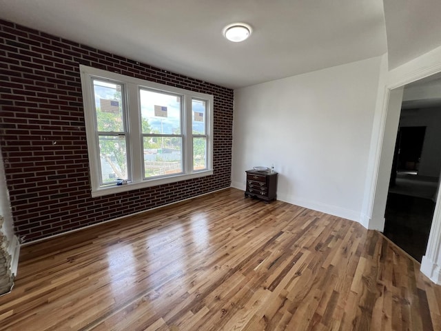 unfurnished room featuring hardwood / wood-style flooring and brick wall