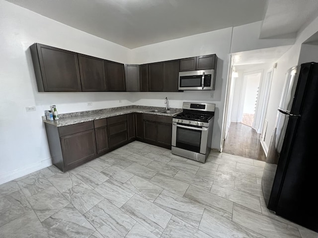 kitchen featuring light stone countertops, appliances with stainless steel finishes, dark brown cabinets, and sink