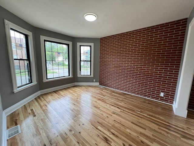 empty room featuring brick wall and light hardwood / wood-style floors