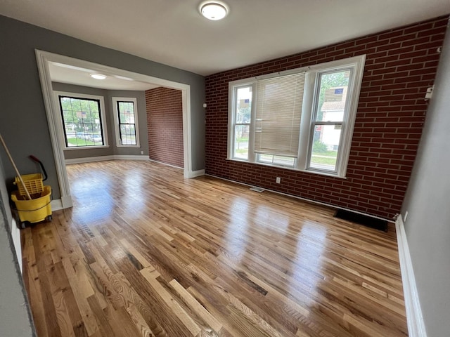 unfurnished room with light hardwood / wood-style floors and brick wall