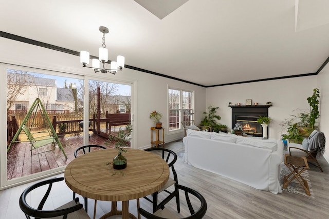 dining space featuring light wood finished floors, baseboards, a glass covered fireplace, crown molding, and a notable chandelier