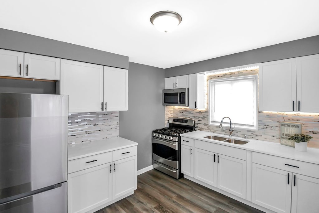 kitchen with backsplash, sink, dark hardwood / wood-style floors, appliances with stainless steel finishes, and white cabinetry