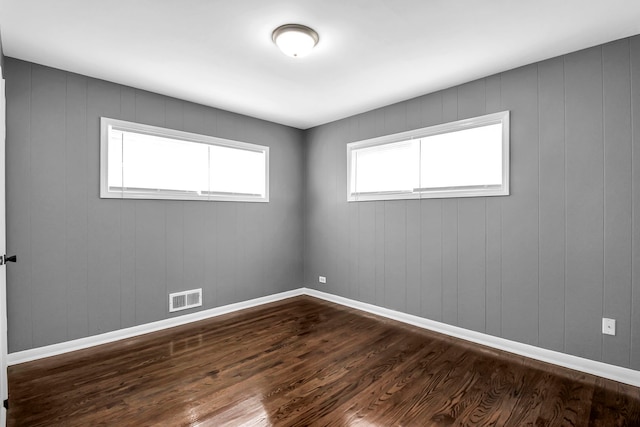 spare room with wood-type flooring, a healthy amount of sunlight, and wood walls