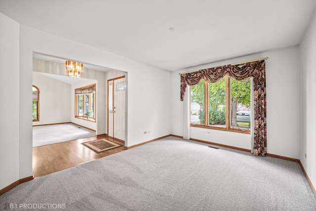 carpeted empty room with a notable chandelier and a wealth of natural light