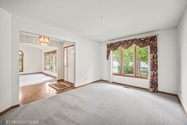 unfurnished room with carpet floors, wood finished floors, visible vents, baseboards, and an inviting chandelier