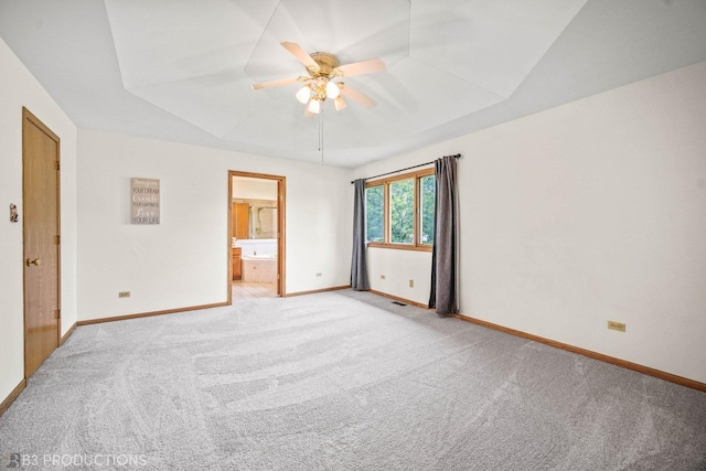 unfurnished bedroom with light carpet, a tray ceiling, ensuite bath, and baseboards