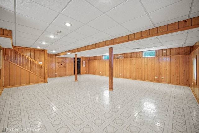 basement featuring light tile patterned flooring, a drop ceiling, and wood walls