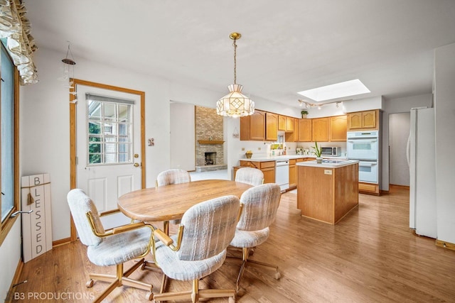 dining space with light wood-type flooring, a skylight, a fireplace, and baseboards