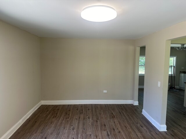 empty room with a notable chandelier and dark wood-type flooring