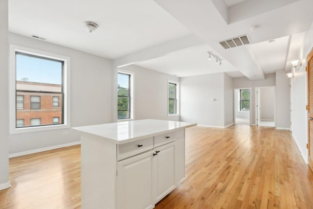 kitchen featuring white cabinetry, light wood-type flooring, track lighting, a kitchen island, and light stone countertops