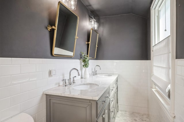 bathroom with double vanity, a sink, a wainscoted wall, and tile walls