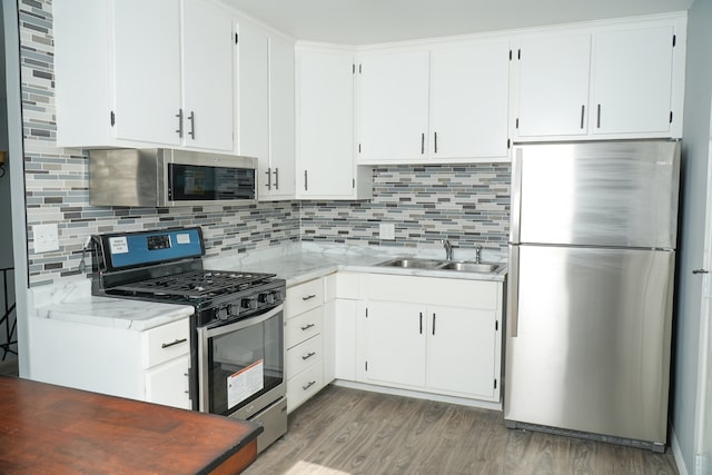 kitchen with tasteful backsplash, hardwood / wood-style floors, sink, stainless steel appliances, and white cabinets