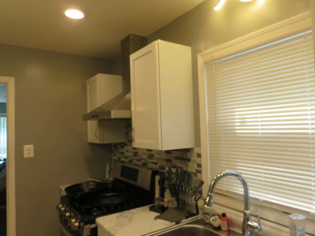 kitchen with white cabinetry, tasteful backsplash, wall chimney exhaust hood, sink, and stove