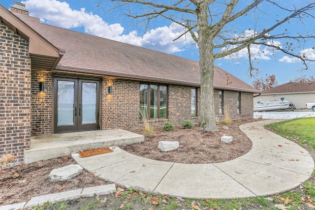 property entrance featuring a shingled roof, french doors, and brick siding