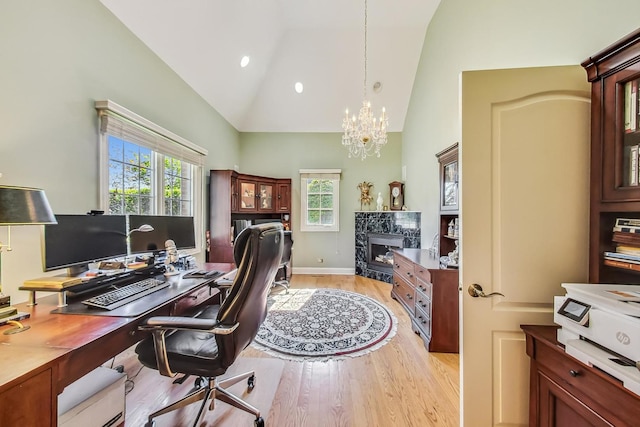 office area featuring a premium fireplace, light hardwood / wood-style flooring, a notable chandelier, and high vaulted ceiling