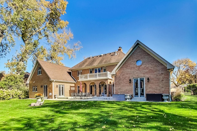 rear view of property featuring a patio, a lawn, and a balcony