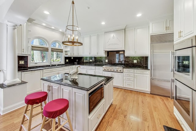 kitchen with a kitchen island, built in appliances, decorative light fixtures, light wood-type flooring, and white cabinetry