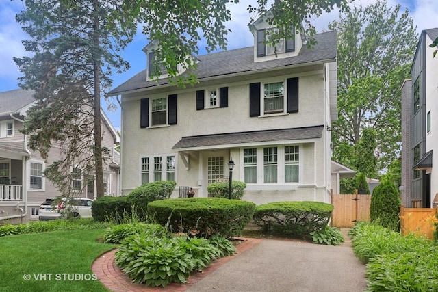 american foursquare style home featuring a shingled roof, stucco siding, fence, and a front lawn