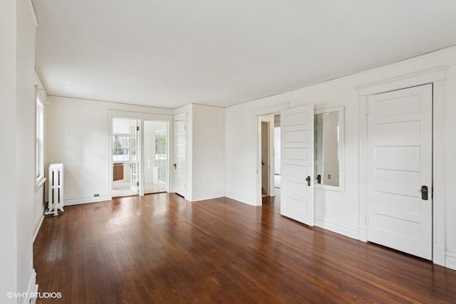 spare room featuring baseboards, dark wood-style flooring, and radiator