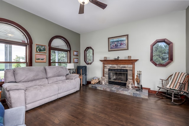 living room with ceiling fan, dark hardwood / wood-style flooring, and a stone fireplace