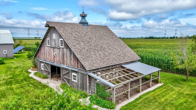 back of property featuring an outdoor structure, a lawn, and a rural view