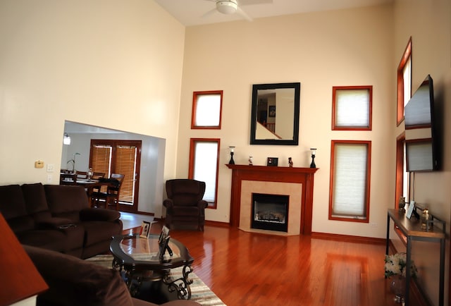 living room featuring ceiling fan, a tiled fireplace, hardwood / wood-style flooring, and a high ceiling