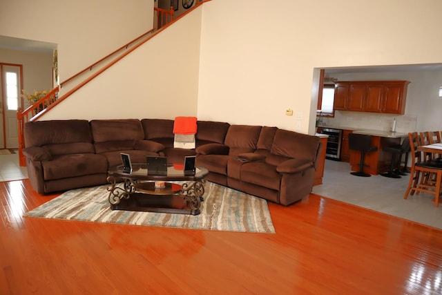 living room with light wood-type flooring, a towering ceiling, and beverage cooler