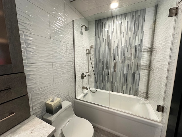 bathroom featuring tile walls, toilet, and shower / bath combination with glass door