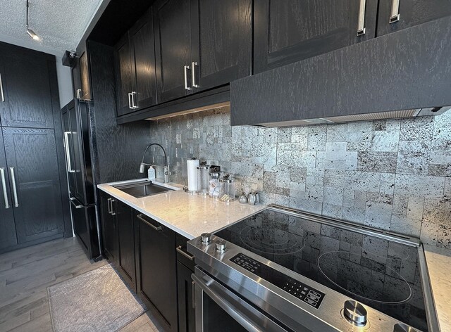 kitchen with a textured ceiling, sink, stainless steel range with electric cooktop, light hardwood / wood-style flooring, and black fridge