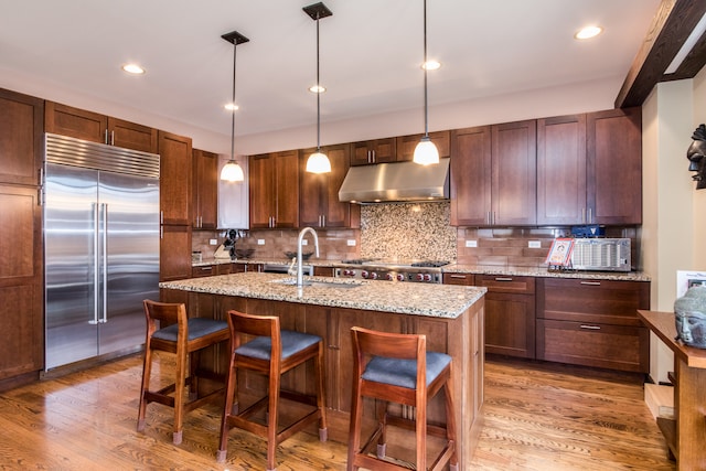 kitchen featuring built in fridge, hanging light fixtures, decorative backsplash, sink, and light hardwood / wood-style floors