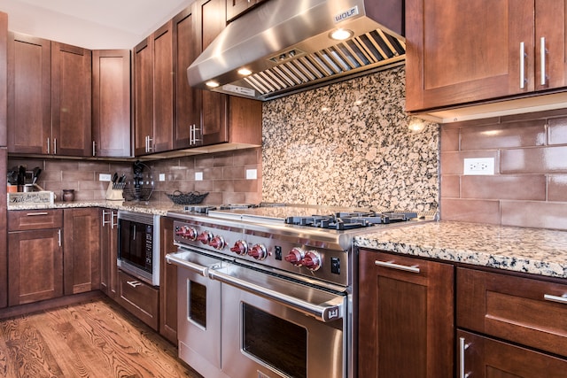 kitchen featuring wall chimney range hood, backsplash, black microwave, light hardwood / wood-style floors, and range with two ovens