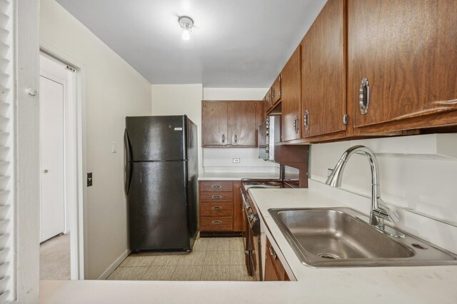 kitchen featuring brown cabinetry, freestanding refrigerator, baseboards, light countertops, and a sink