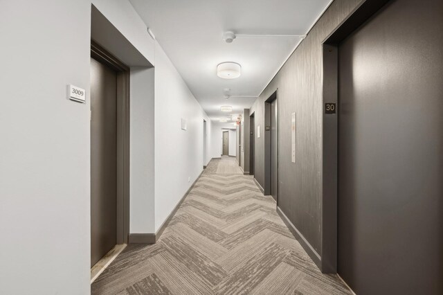 corridor featuring baseboards, light carpet, and elevator