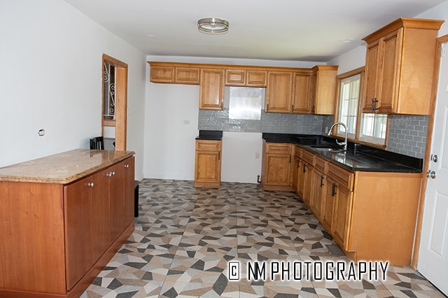 kitchen featuring dark stone counters, backsplash, sink, and light tile patterned floors