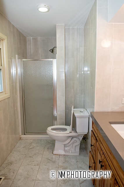 bathroom with vanity, tile patterned floors, tile walls, an enclosed shower, and toilet