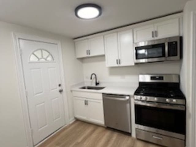 kitchen featuring white cabinets, light wood-type flooring, stainless steel appliances, and sink