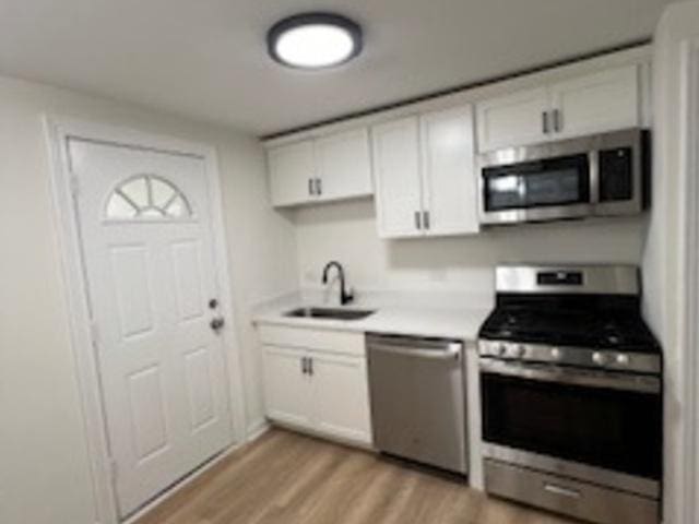 kitchen with sink, stainless steel appliances, white cabinets, and light wood-type flooring