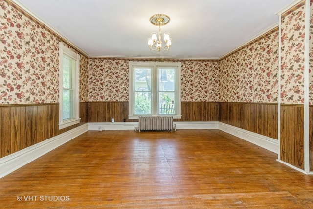 unfurnished room featuring radiator, ornamental molding, wooden walls, a chandelier, and hardwood / wood-style flooring