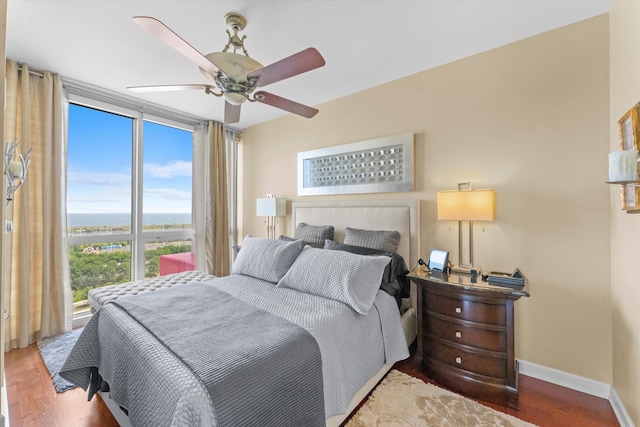 bedroom with wood-type flooring, a water view, and ceiling fan